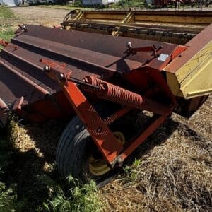 Rusty hay baler attachment on a wheeled red frame resting on a dry field.