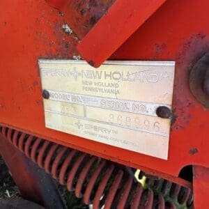 Metal identification plate on a red Sperry New Holland agricultural machine showing 'Model No.' and 'Serial No.' with worn numbers nearby.