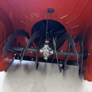 Rear view of red agricultural implement with black curved discs and central hitch, resting on a concrete floor