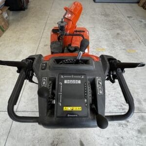 Top-down view of a Husqvarna snow blower with orange intake housing and black control panel in a workshop.