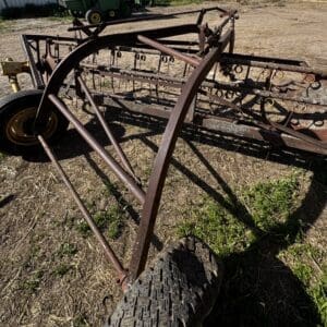 Rusty metal farming implement with wheels and multiple tines lying on a dry field; appears abandoned in a rural area.