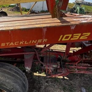 Red Stackliner 1032 agricultural implement parked outdoors, showing hoses and rusted metal frames on a dirt surface.