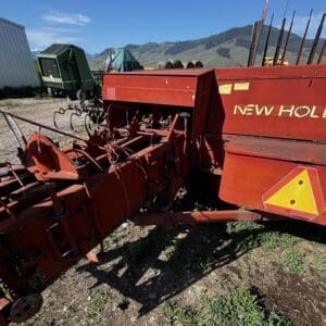 Red New Holland agricultural implement with a plow frame, parked on dirt with mountains in the background (informational, shows machinery used for tilling).