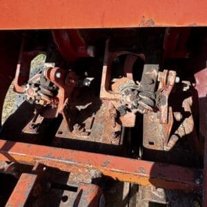 Close-up of rusted tractor hitch linkage with worn bolts and clamps on an orange metal frame.