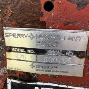 Close-up of a rusted red machine with a metal nameplate reading Sperry New Holland, Model No. 425, Serial No. 530755 (Made in USA).