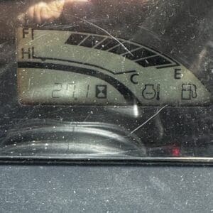 Close-up of a car dashboard fuel gauge showing level near empty (needle near E) and a mid-range engine temperature gauge with small warning icons visible on the panel.