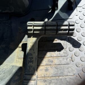 Close-up of a dusty vehicle foot pedal assembly on a ribbed floor mat, showing the accelerator pedal.