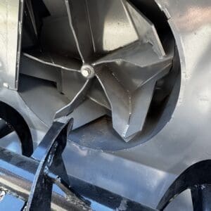 Close-up of a large industrial blower/impeller with curved metal blades inside a circular housing, mounted on a frame.
