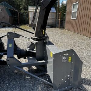 Large industrial wood chipper attachment outdoors, with a tall angled black chute and gray base housing, on a gravel area near buildings.