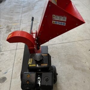 Red PTO-powered wood chipper with a large angled chute for feeding branches, outdoors on a concrete surface