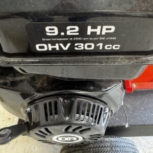 Close-up of a black engine with a prominent label reading '9.2 HP OHV 301cc' and a DR-branded recoil starter, with a tire visible in the foreground.