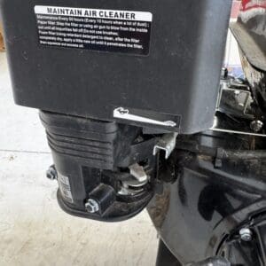 Close-up of an outboard motor's air cleaner housing with a maintenance label reading 'MAINTAIN AIR CLEANER' visible.