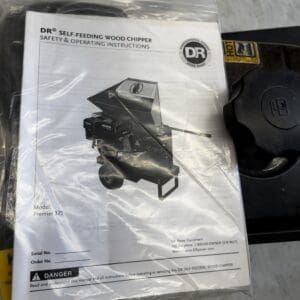 Manual for a DR Self-Feeding Wood Chipper (Premier 375) inside a plastic bag, photographed on a workshop floor.