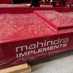 Red industrial machinery with a white 'machina IMPLEMENTS' logo, resting on a wooden block in a workshop setting.